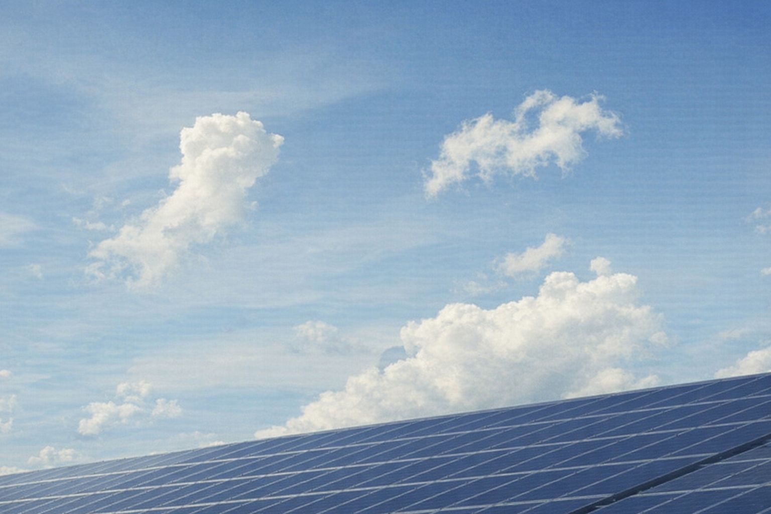 Aurinkopaneelit sinisellä taivaalla ja valkoisilla pilvillä, symboloiden uusiutuvaa energiaa.